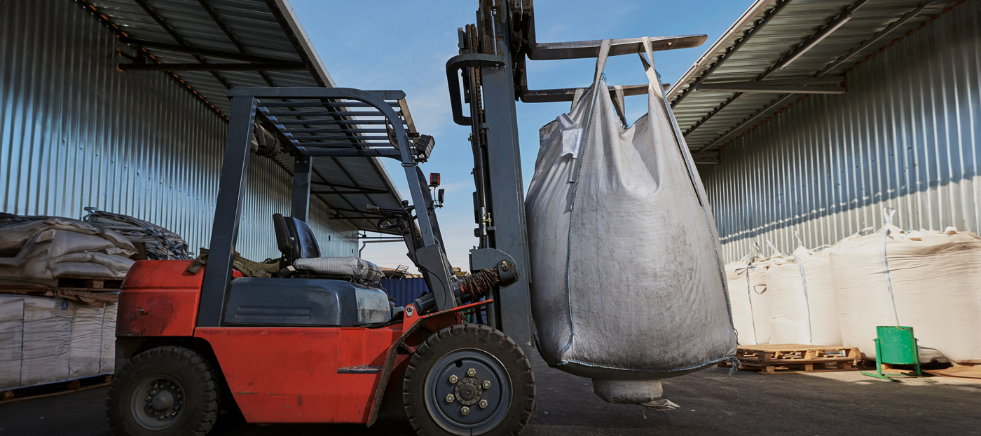 Roter Gabelstapler hebt Big Bag vor Industriehalle
