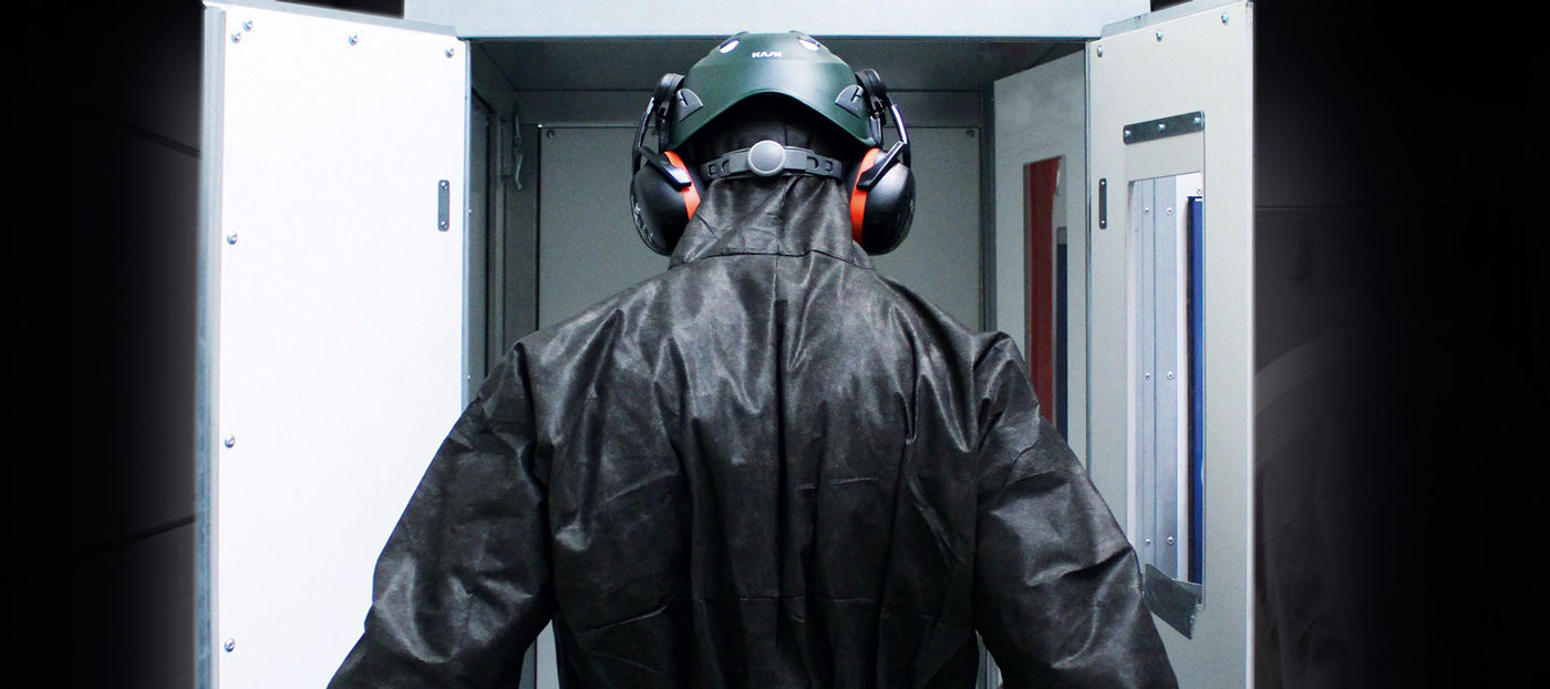 Person mit Schutzhelm und Gehörschutz betritt industrielle Kammer